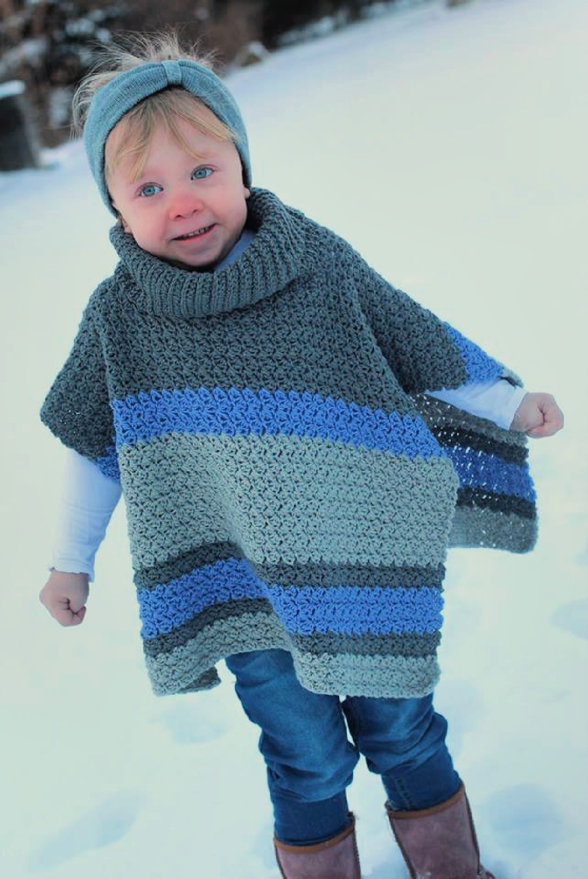 A child wearing a gray and blue colored poncho playing in the snow.