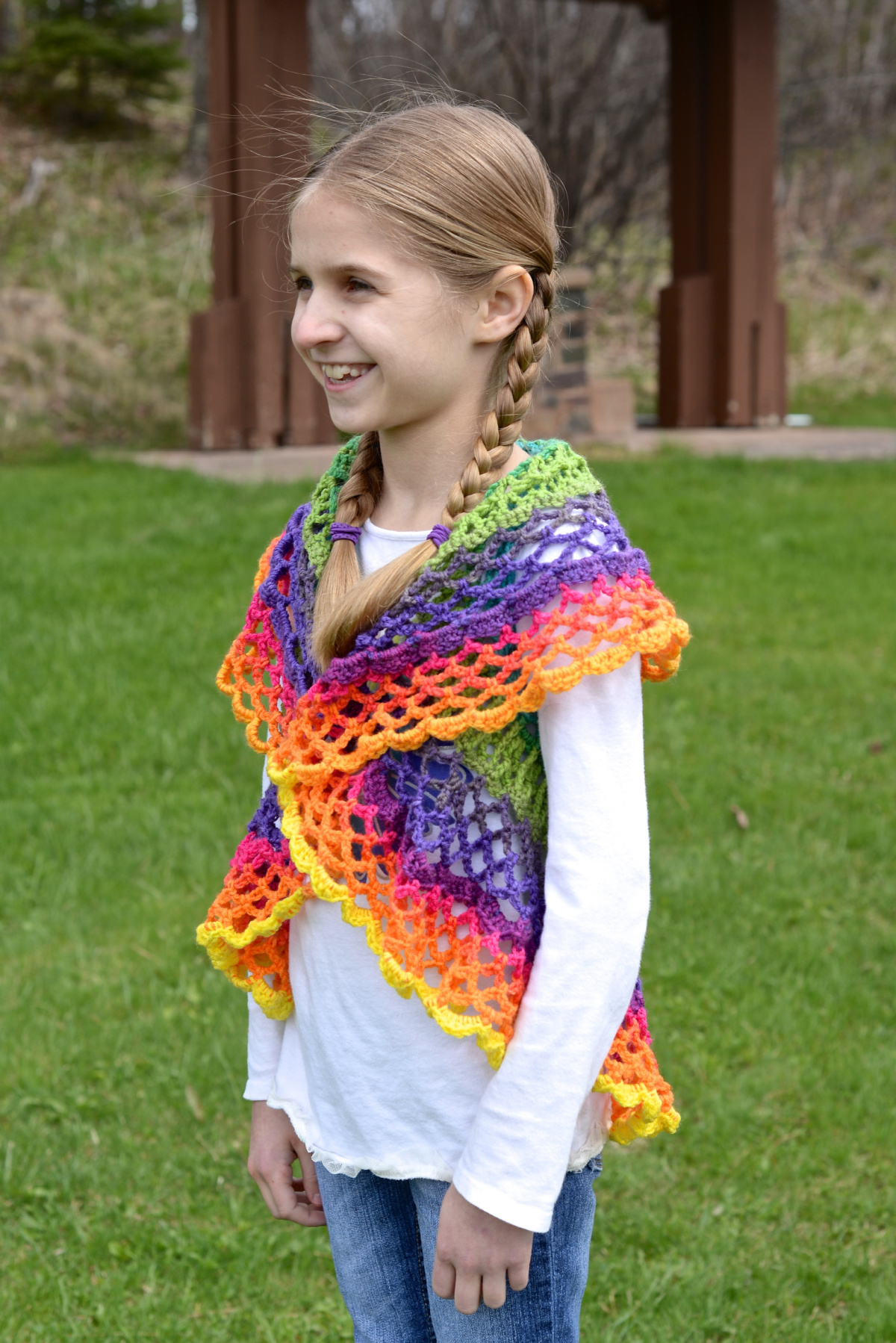 Girl wearing a colorful mandala crochet vest, jeans, and a white shirt standing outside.