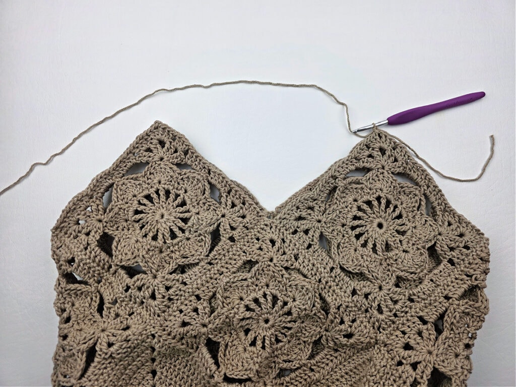 A crochet hook working the edging of a crochet granny square bag.