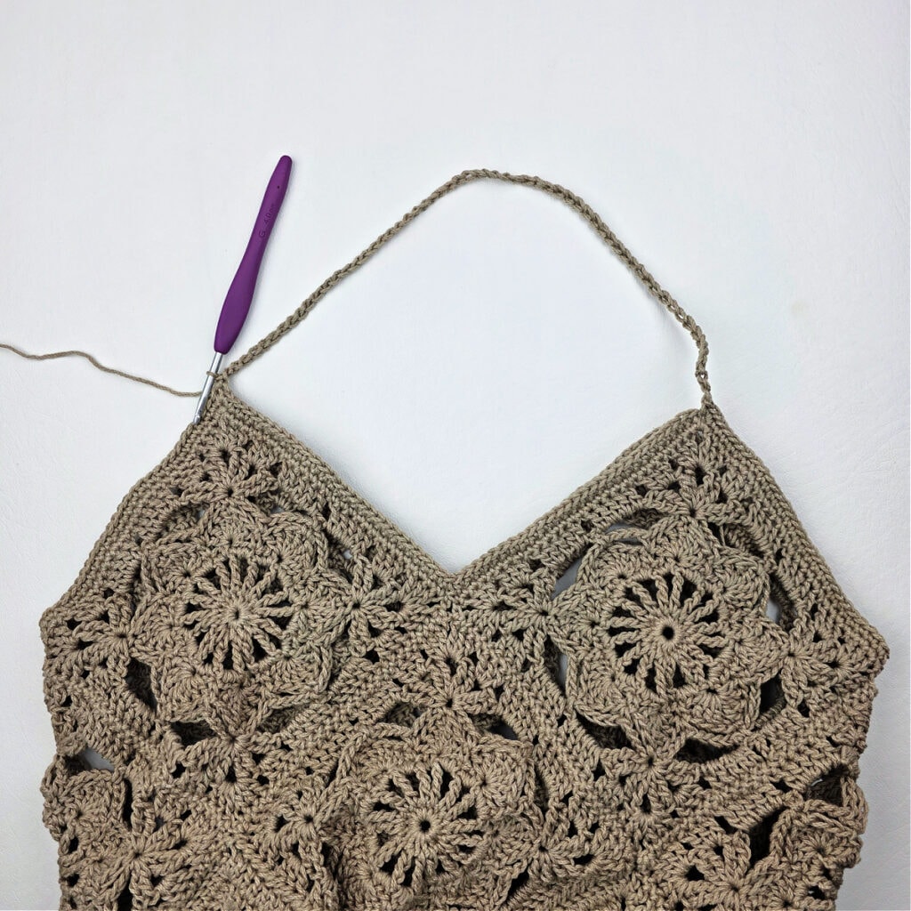 A crochet hook working the strap of a crochet granny square bag.
