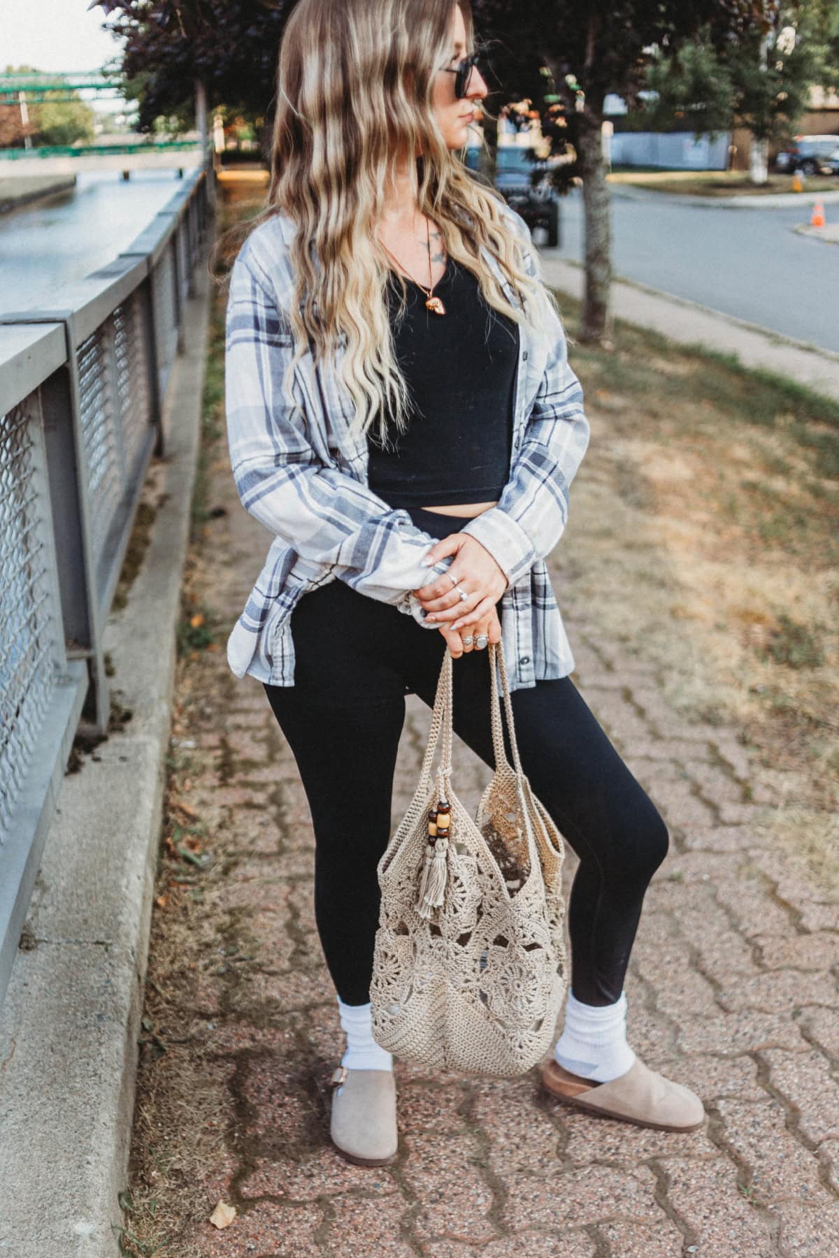 A girl holding a crochet granny squares bag with her knee bent, standing next to a fence.