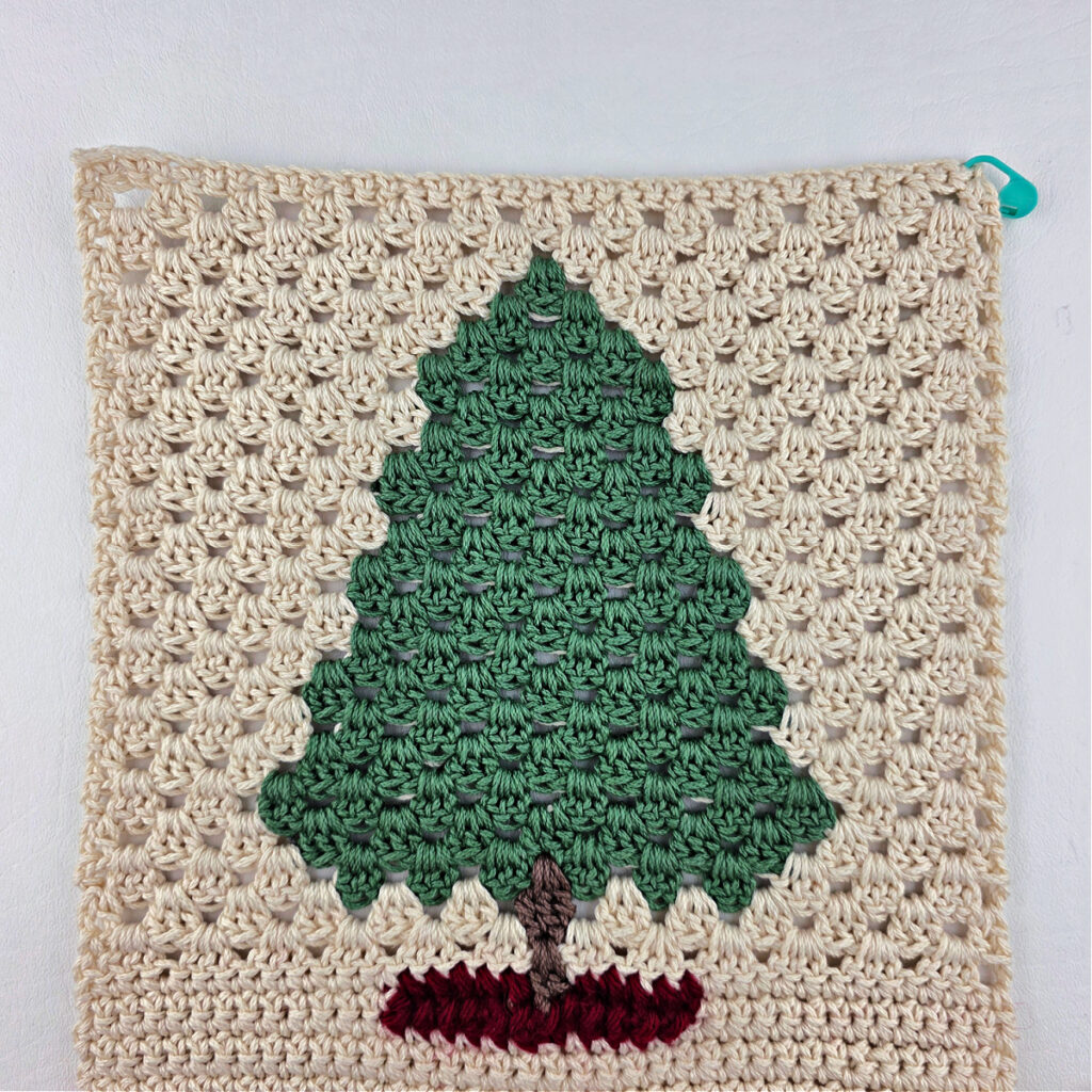 A fir tree made from green and brown yarn against a white background.