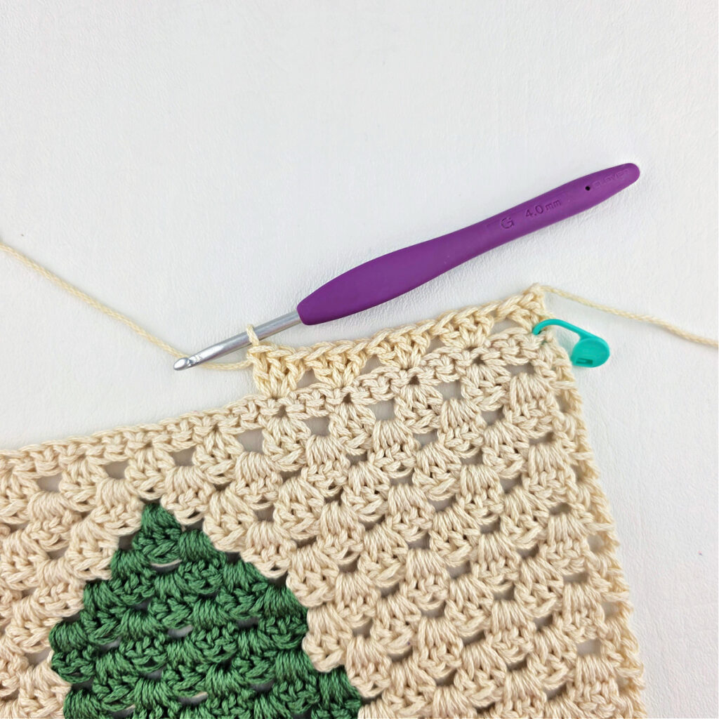 Making stitches with cream colored yarn and a purple crochet hook.