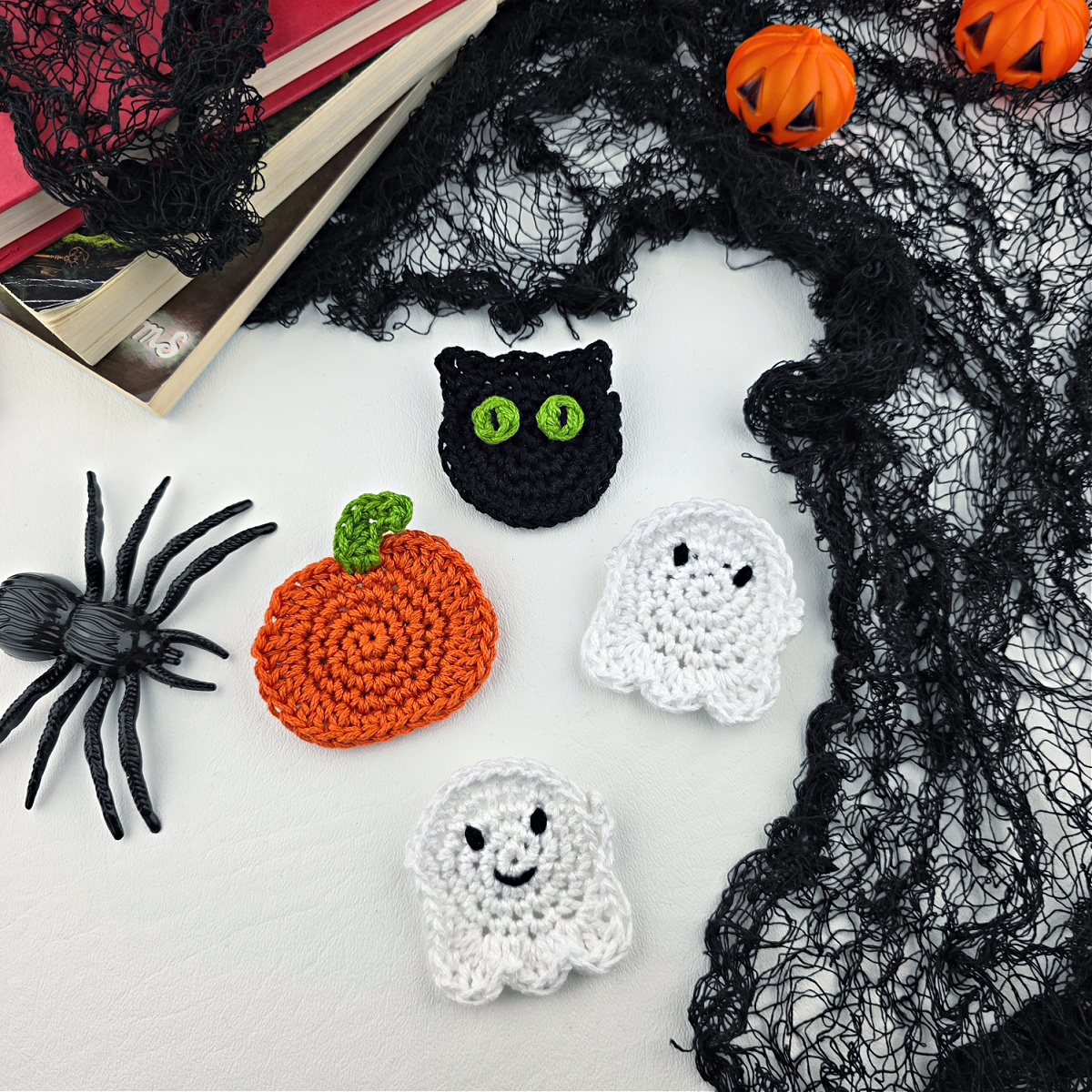 A crochet pumpkin, cat, and two ghosts next to a spider and black net.