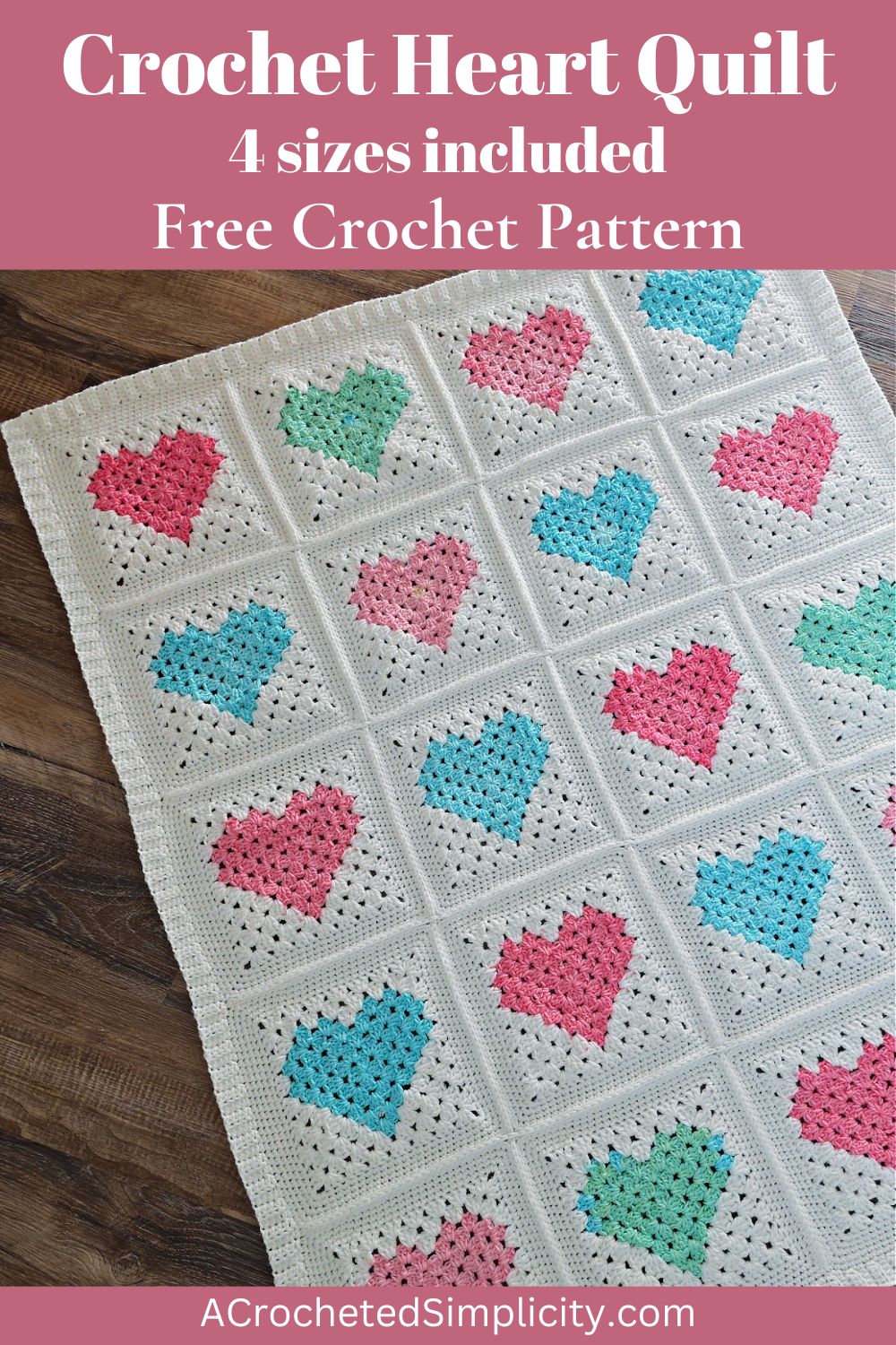White crochet quilt made from pink and blue heart motifs spread out on a wooden floor.