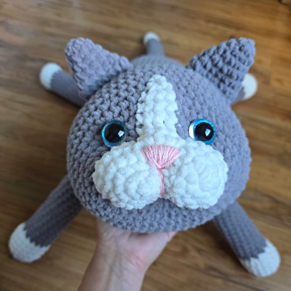 In process of assembling a crochet cat laying against a wooden floor.