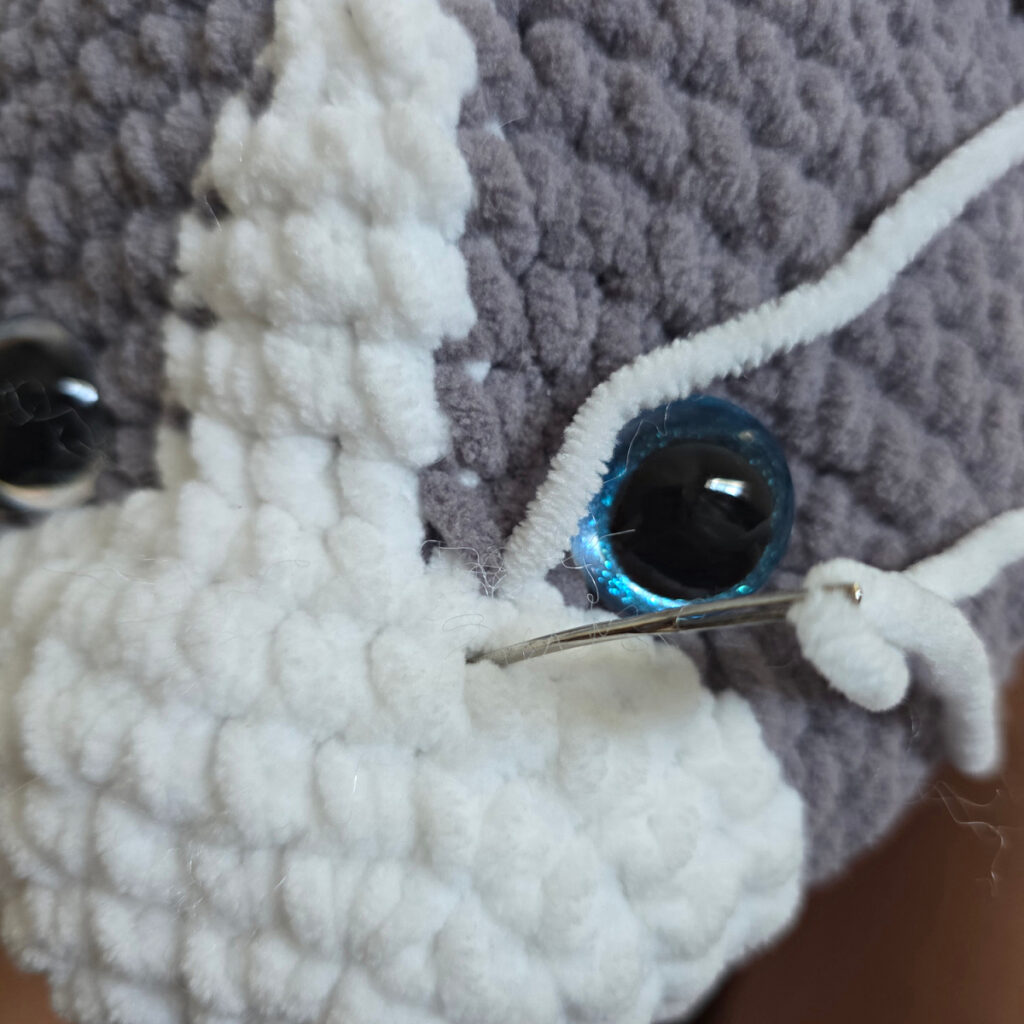 In process of assembling a crochet cat laying against a wooden floor.