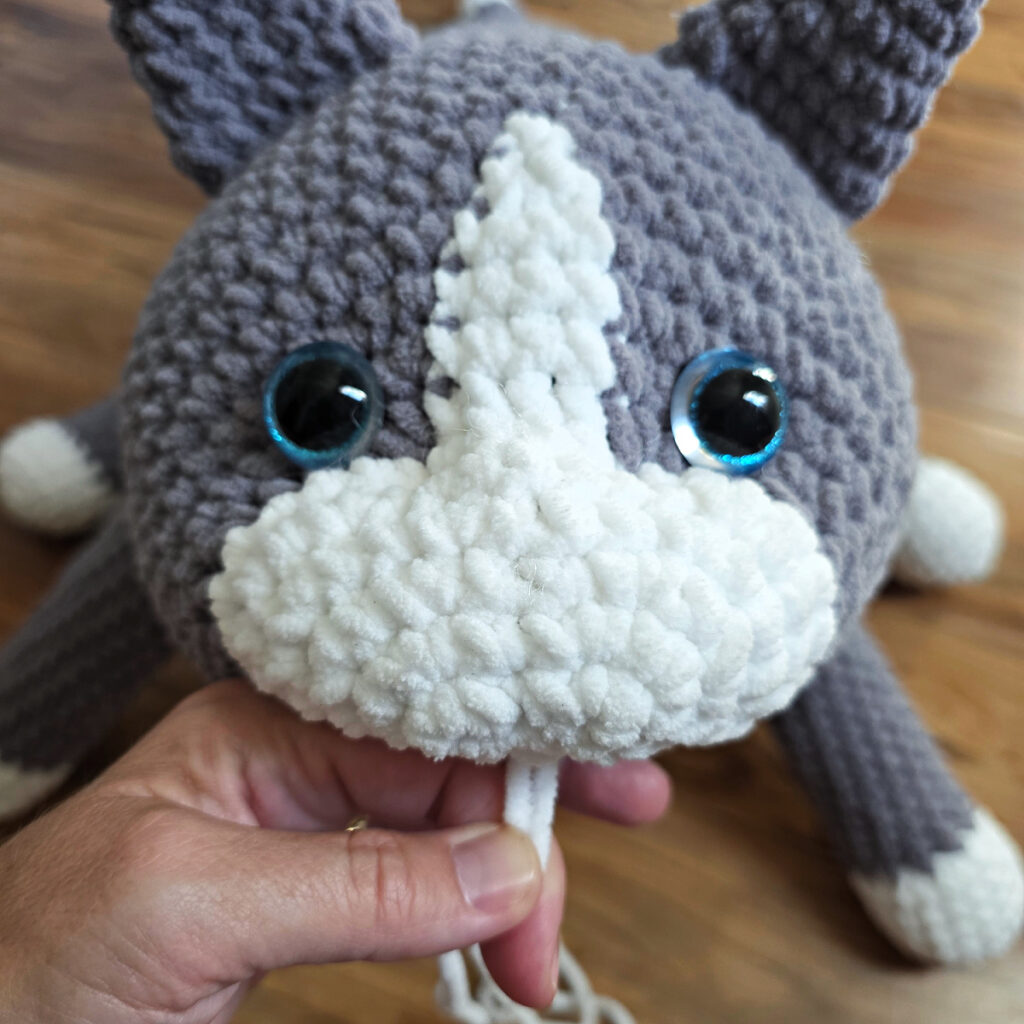 In process of assembling a crochet cat laying against a wooden floor.