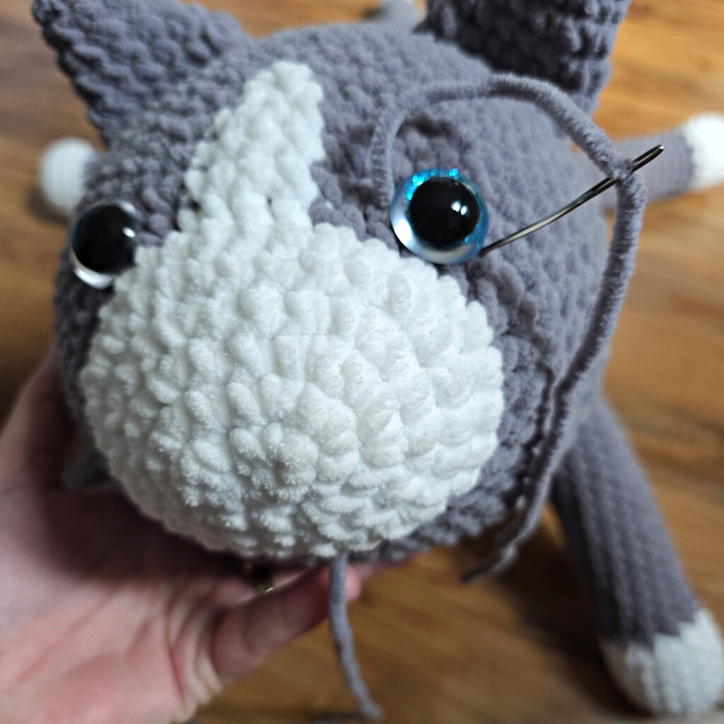 In process of assembling a crochet cat laying against a wooden floor.