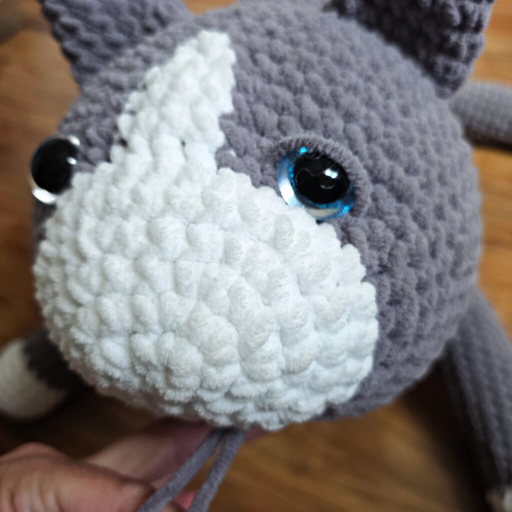 In process of assembling a crochet cat laying against a wooden floor.