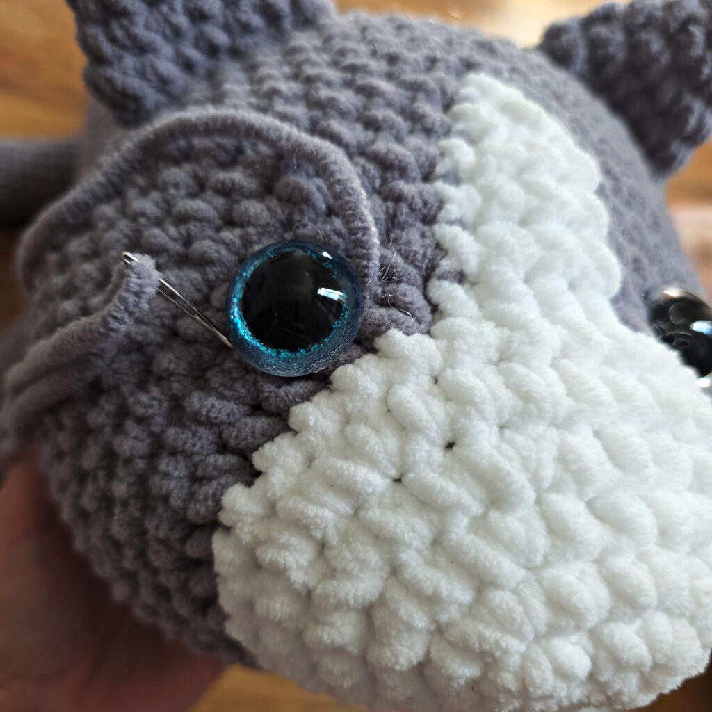 In process of assembling a crochet cat laying against a wooden floor.
