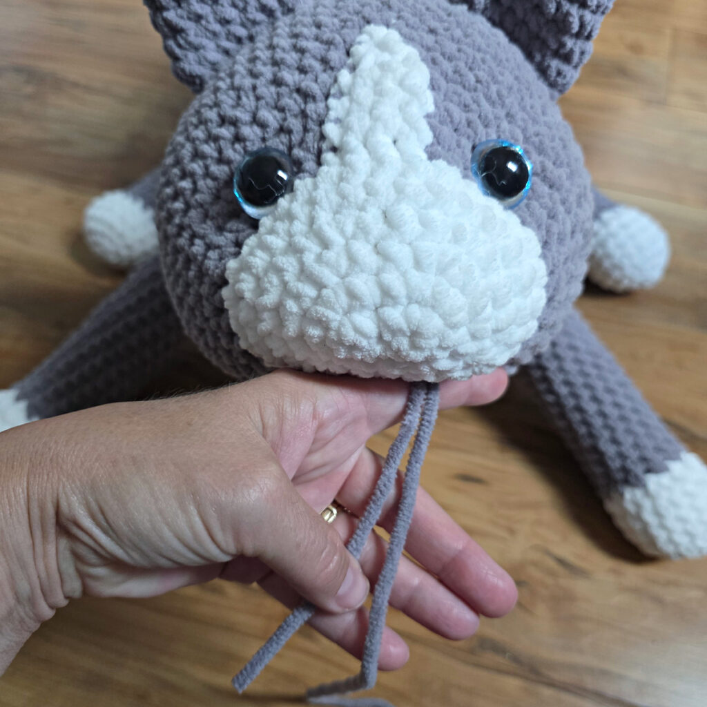 In process of assembling a crochet cat laying against a wooden floor.