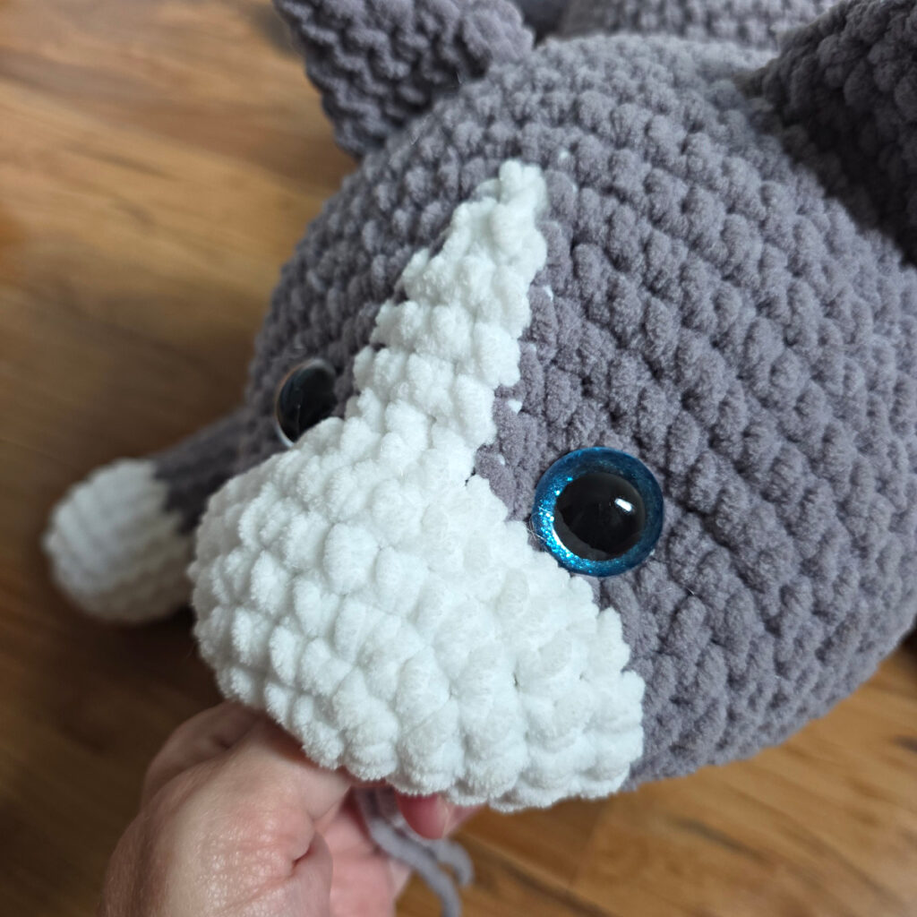 In process of assembling a crochet cat laying against a wooden floor.