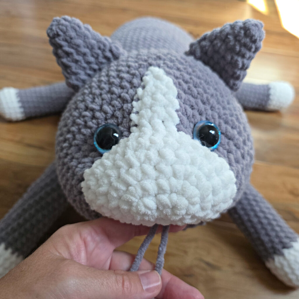In process of assembling a crochet cat laying against a wooden floor.