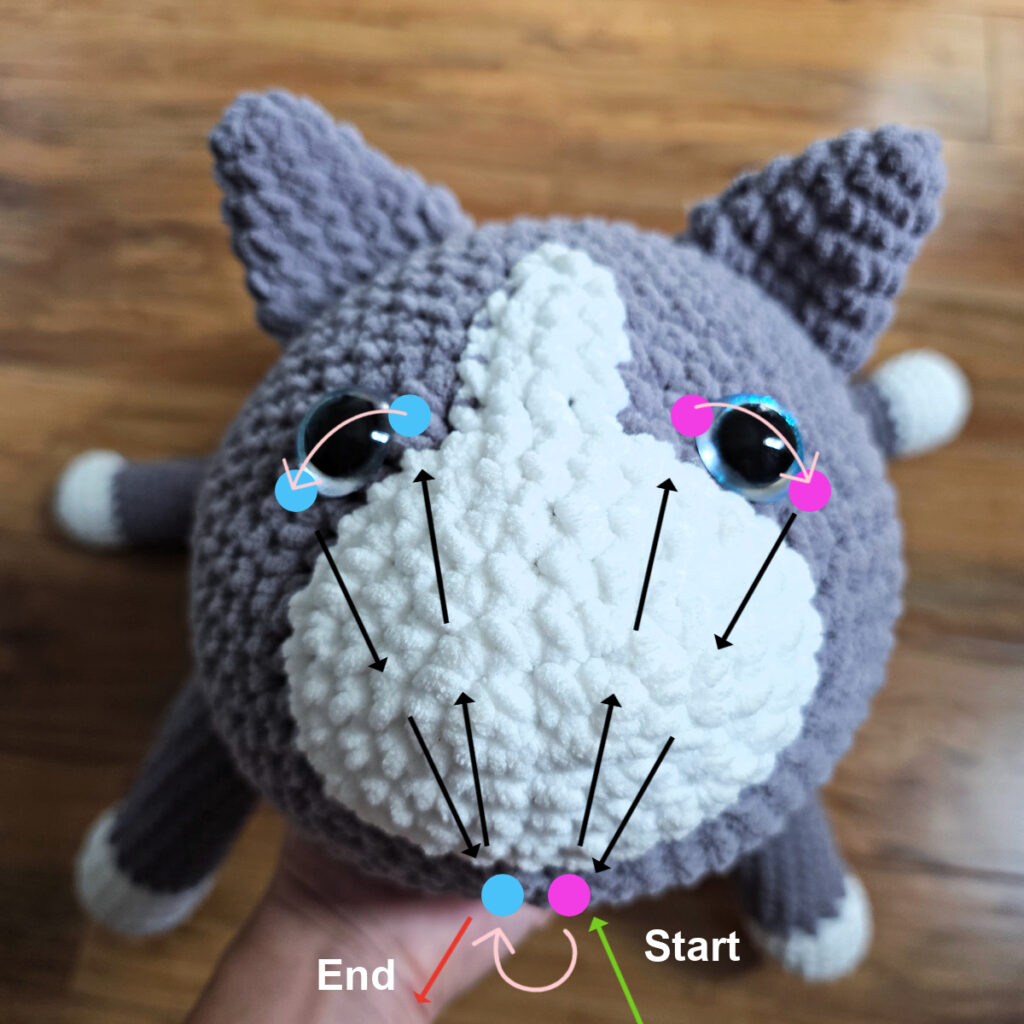 In process of assembling a crochet cat laying against a wooden floor.