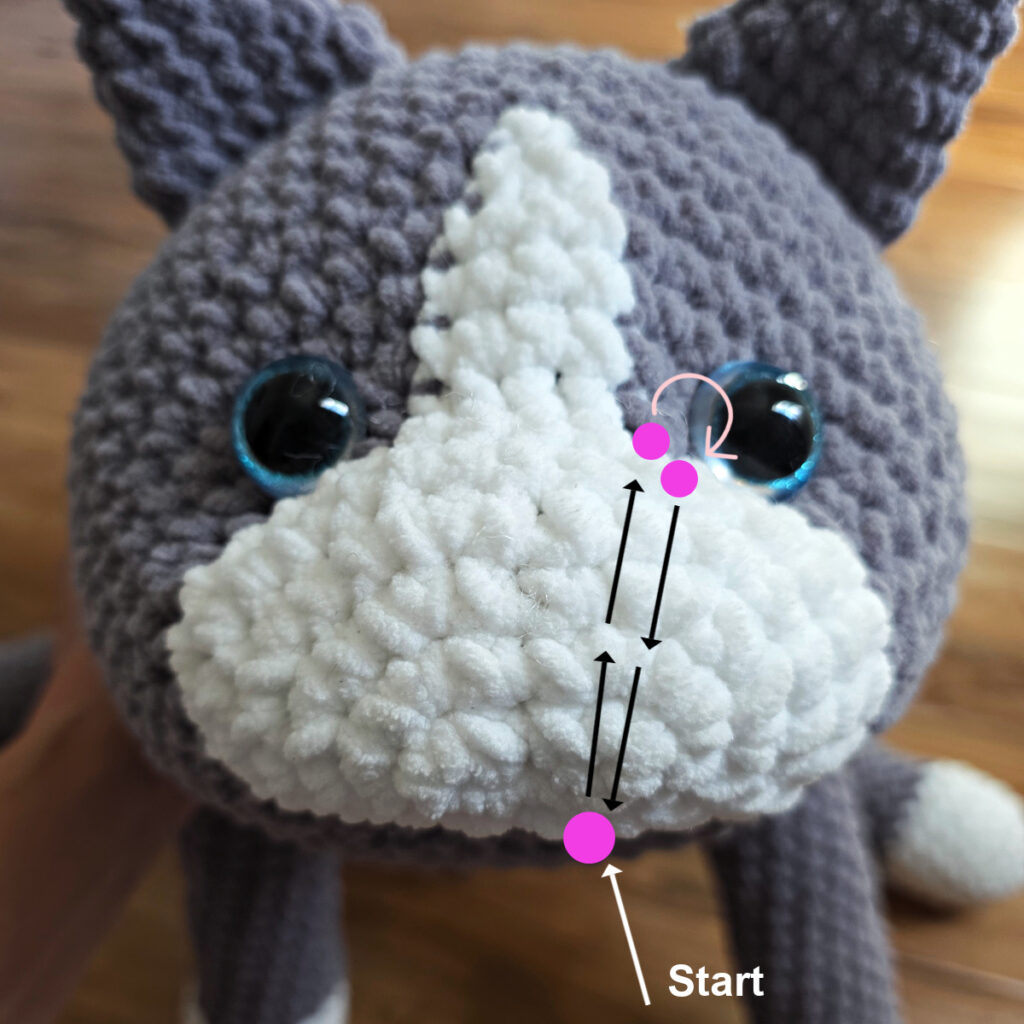 In process of assembling a crochet cat laying against a wooden floor.