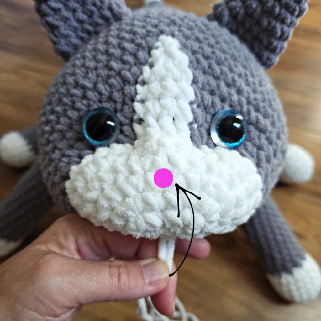 In process of assembling a crochet cat laying against a wooden floor.