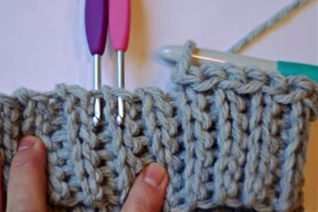 Purple and pink crochet hooks indicating stitches for a slip stitch hat band with a blue crochet hook inserted into a loop.