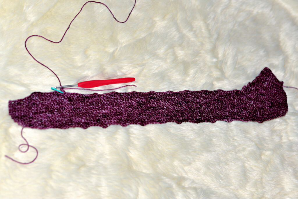 A purple crochet stitch with a red crochet hook against a white background.