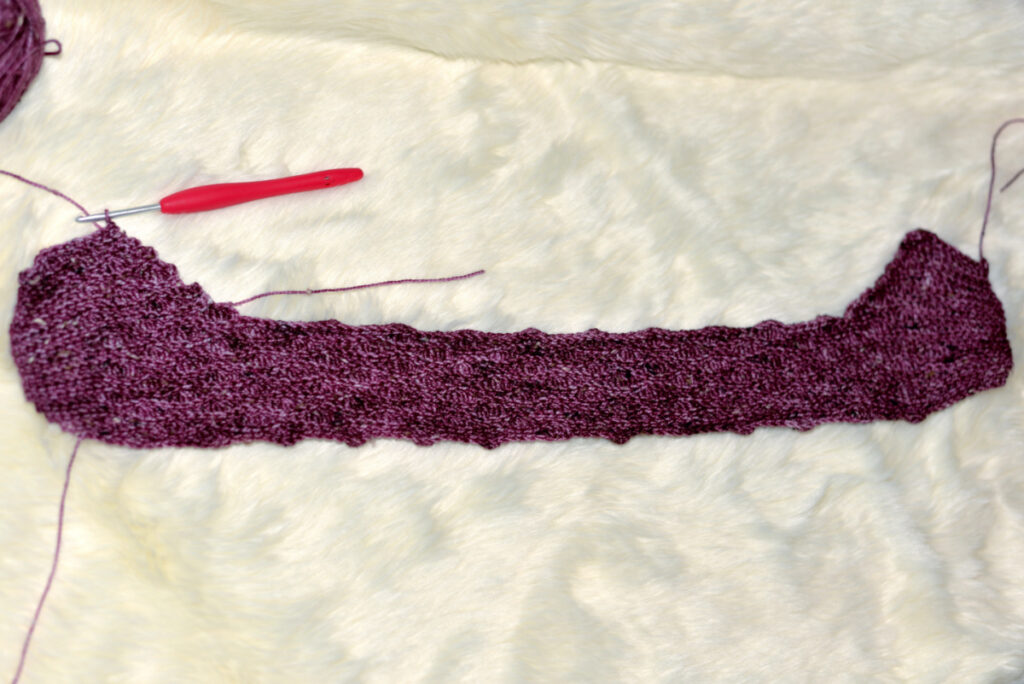 A purple crochet stitch with a red crochet hook and purple ball of yarn in the corner against a white background.