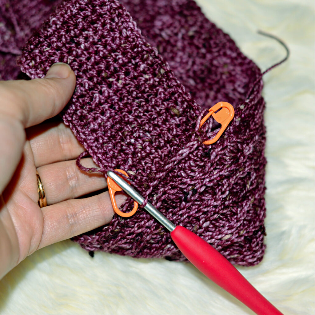 Stitching a purple crochet kimono slipper with two orange stitch markers and a red crochet hook.