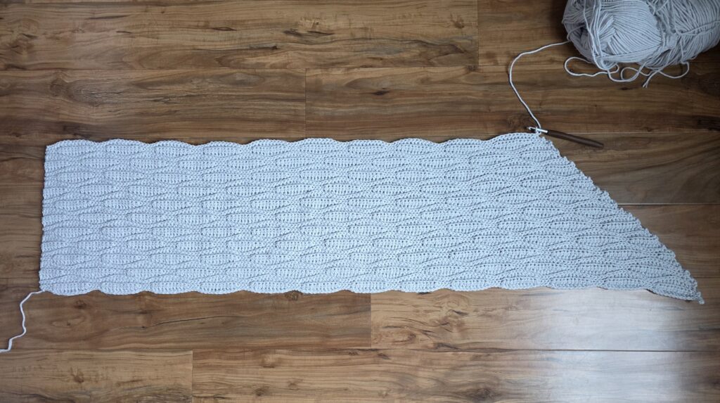A grey crochet shawl spread across a wooden floor.