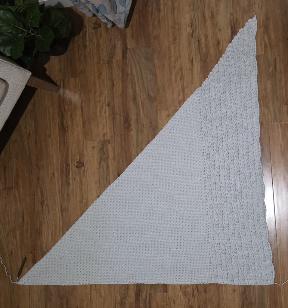 A grey crochet shawl spread across a wooden floor.