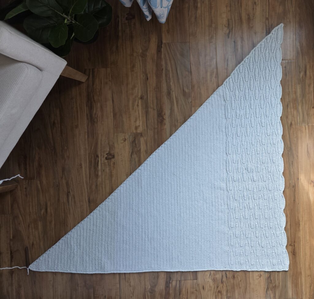 A grey crochet shawl spread across a wooden floor.