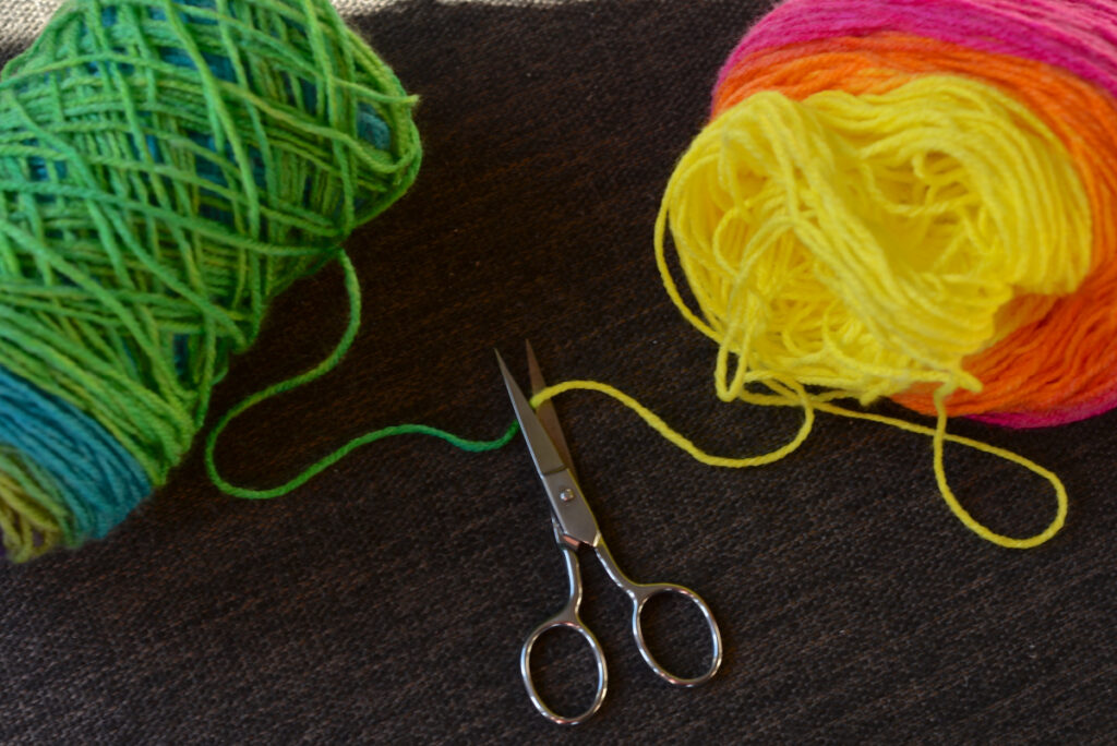 Cutting a cake of Lion Brand Mandala yarn in shade Gnome.