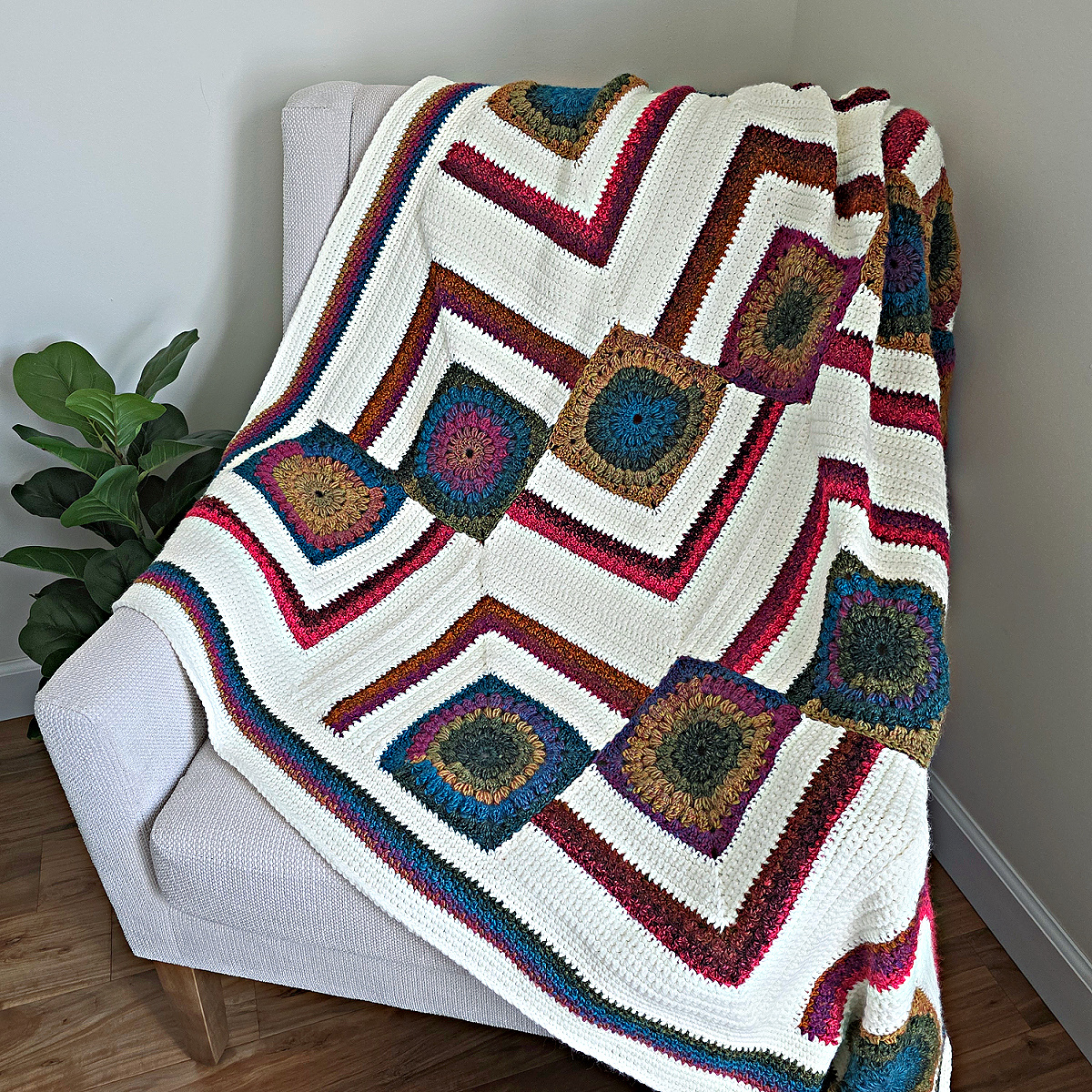 A colorful modern crochet blanket pattern free spread across a sofa with a plant next to it.