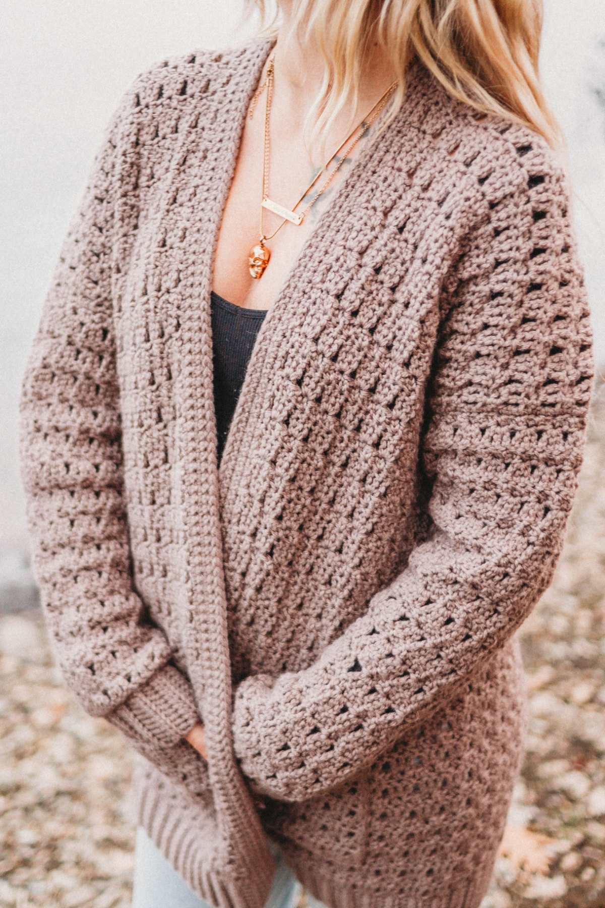 A woman wearing a black top and brown crochet cardigan sweater.