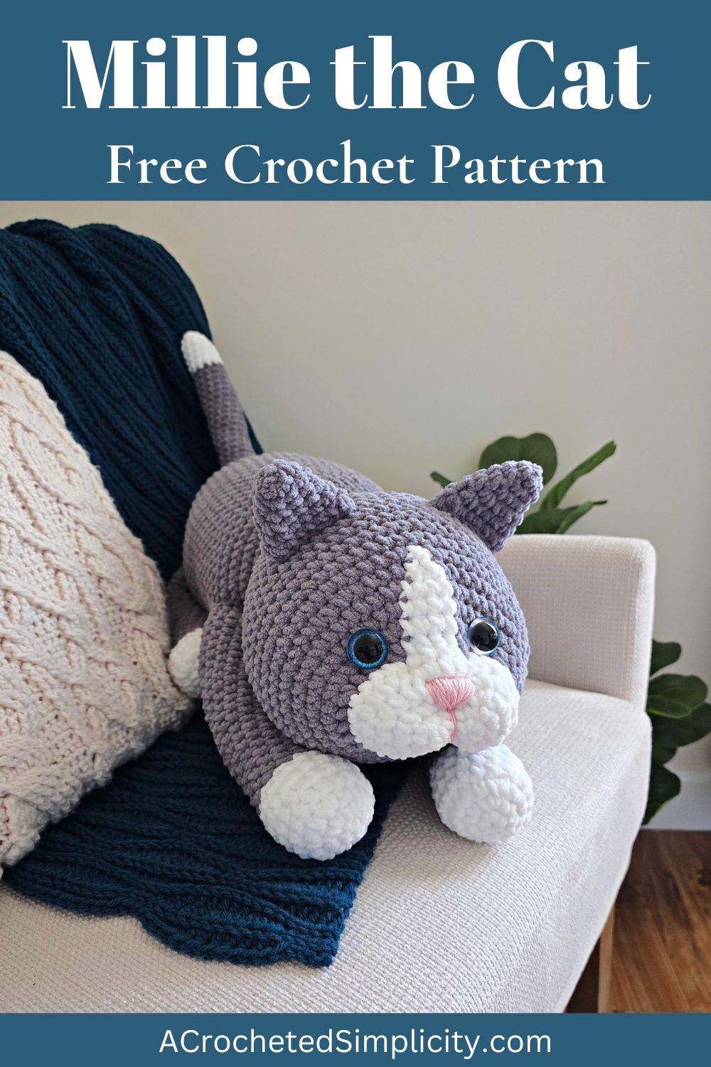 A large gray amigurumi cat on a blue blanket spread on a sofa with a plant next to it.