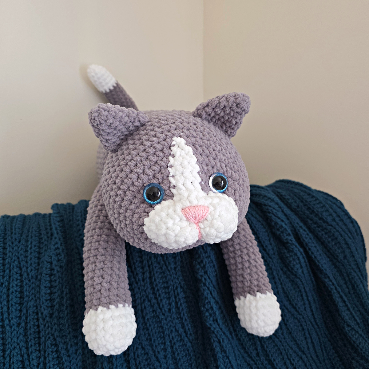 A large gray and white crochet cat on a blue blanket.