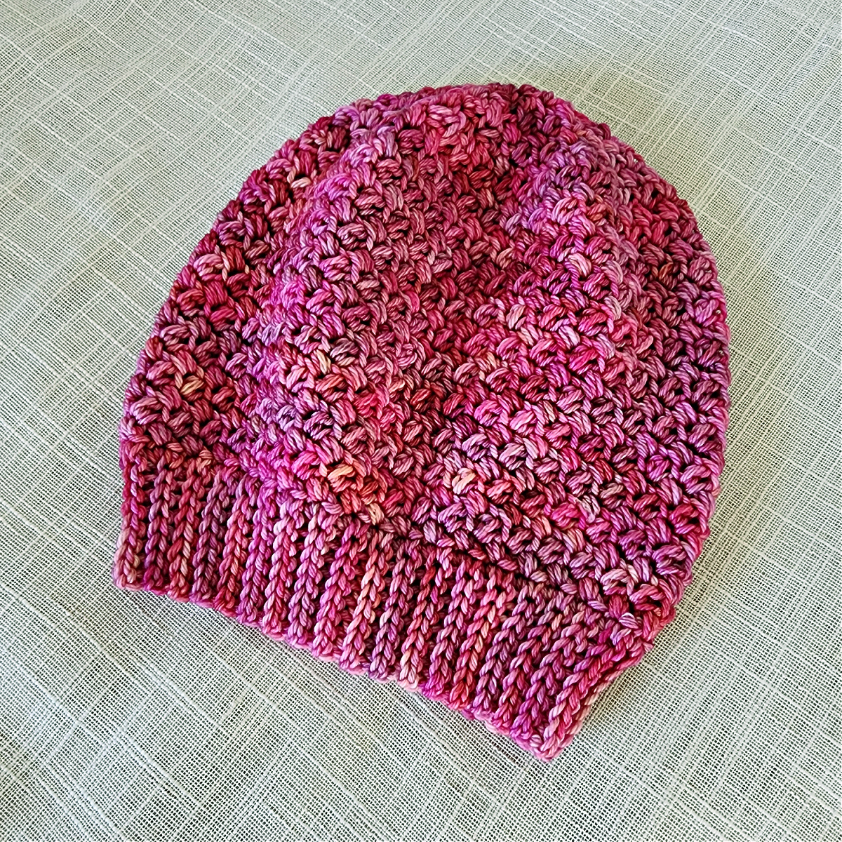 A pink crochet beanie on a plain background.
