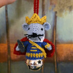 Nutcracker Mouse King crochet ornament being held in front of a painting in the woods.