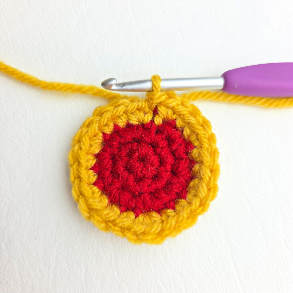 Small red crocheted circle with gold yarn around the edge.