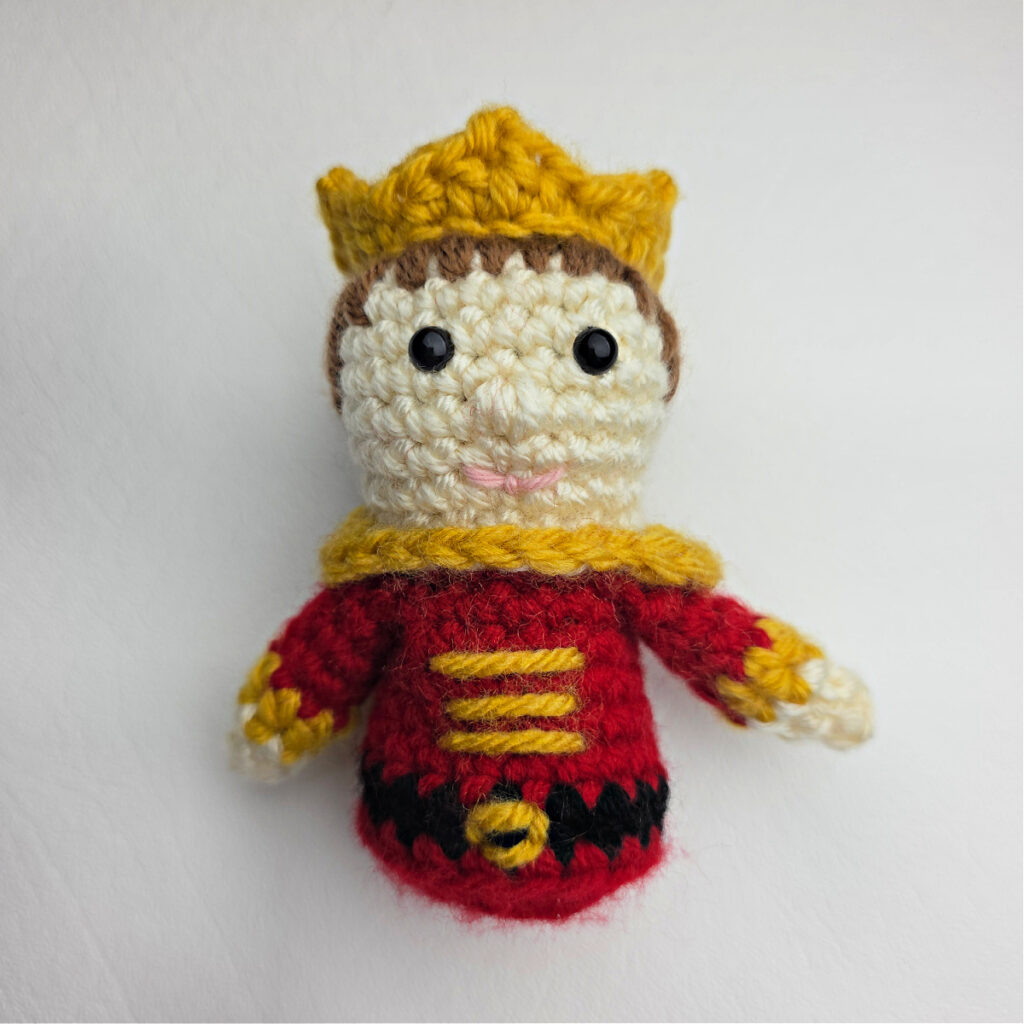 A crochet nutcracker prince ornament wearing a crochet crown.
