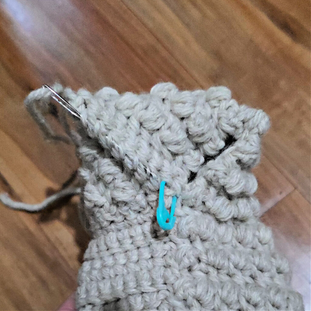 Seaming a grey crochet slipper against a wooden floor.