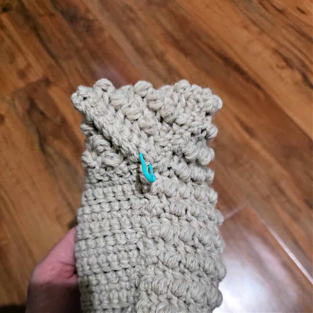 Seaming a grey crochet slipper against a wooden floor.