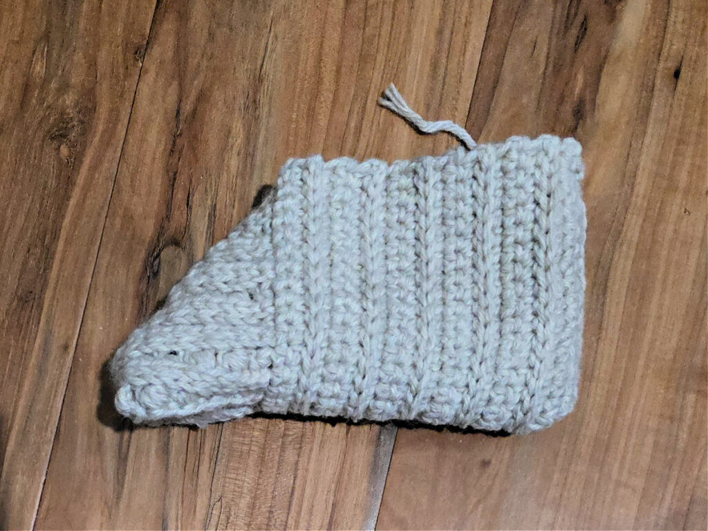 Seaming a grey crochet slipper against a wooden floor.