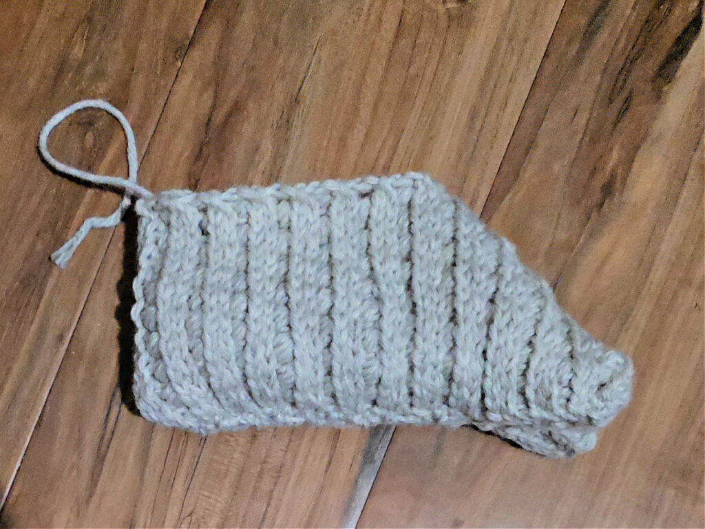 Seaming a grey crochet slipper against a wooden floor.