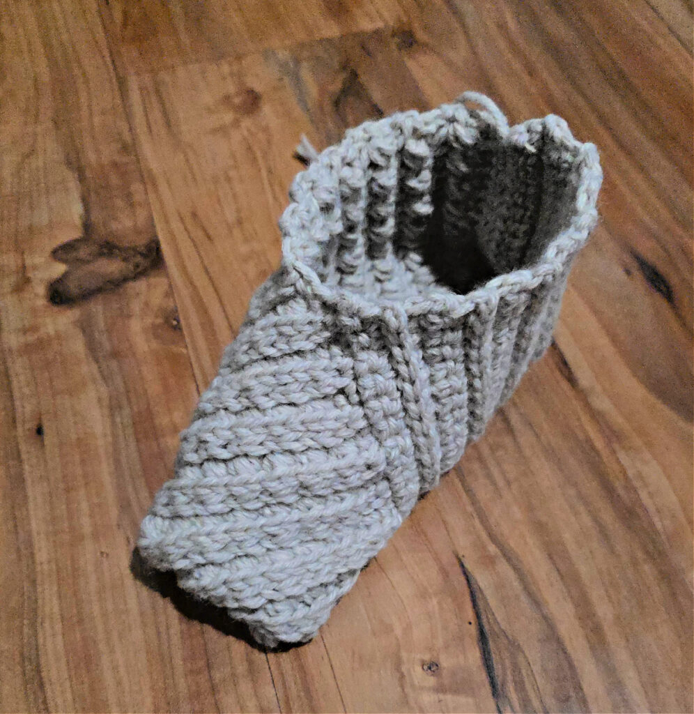 A grey crochet slipper on a wooden floor.