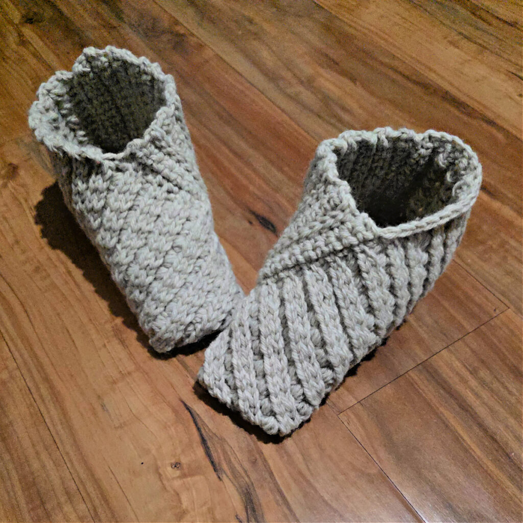 Grey crochet slippers on a wooden floor.