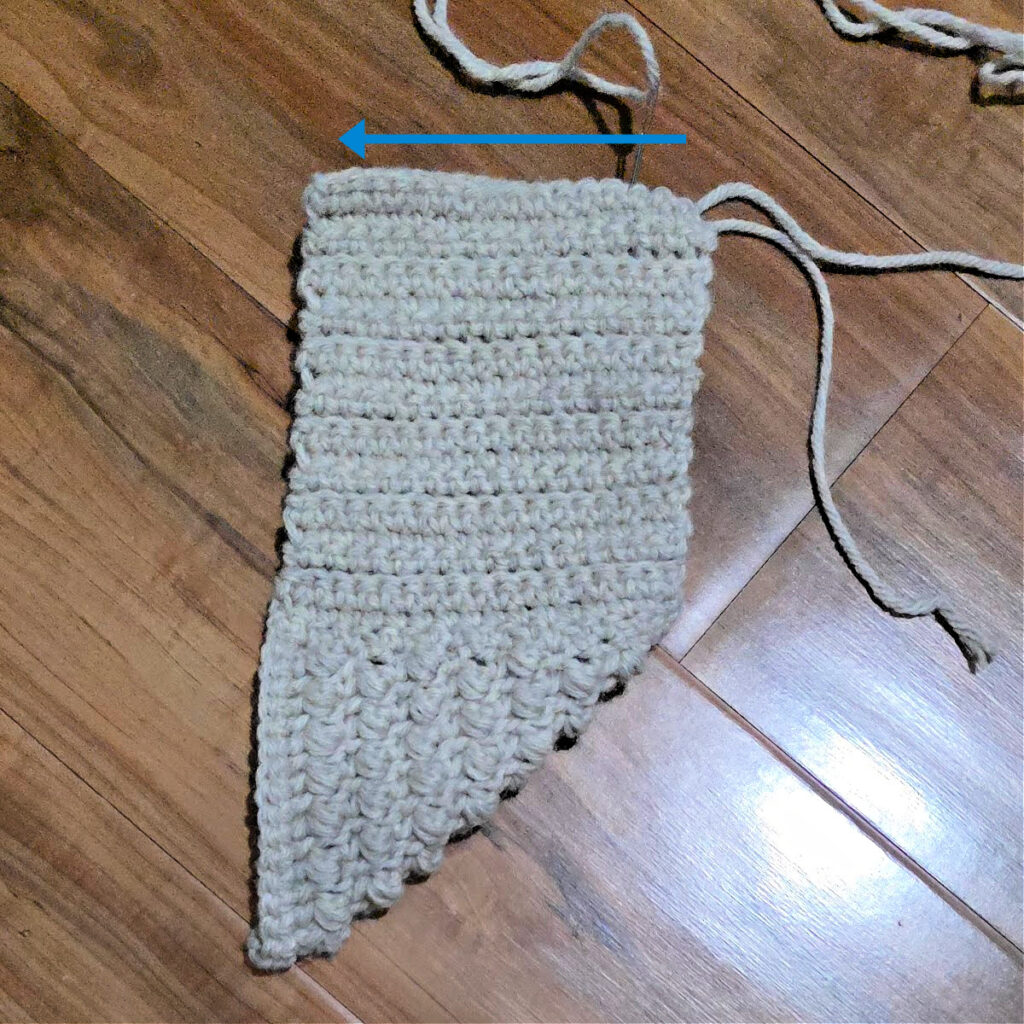 Seaming a grey crochet slipper against a wooden floor.