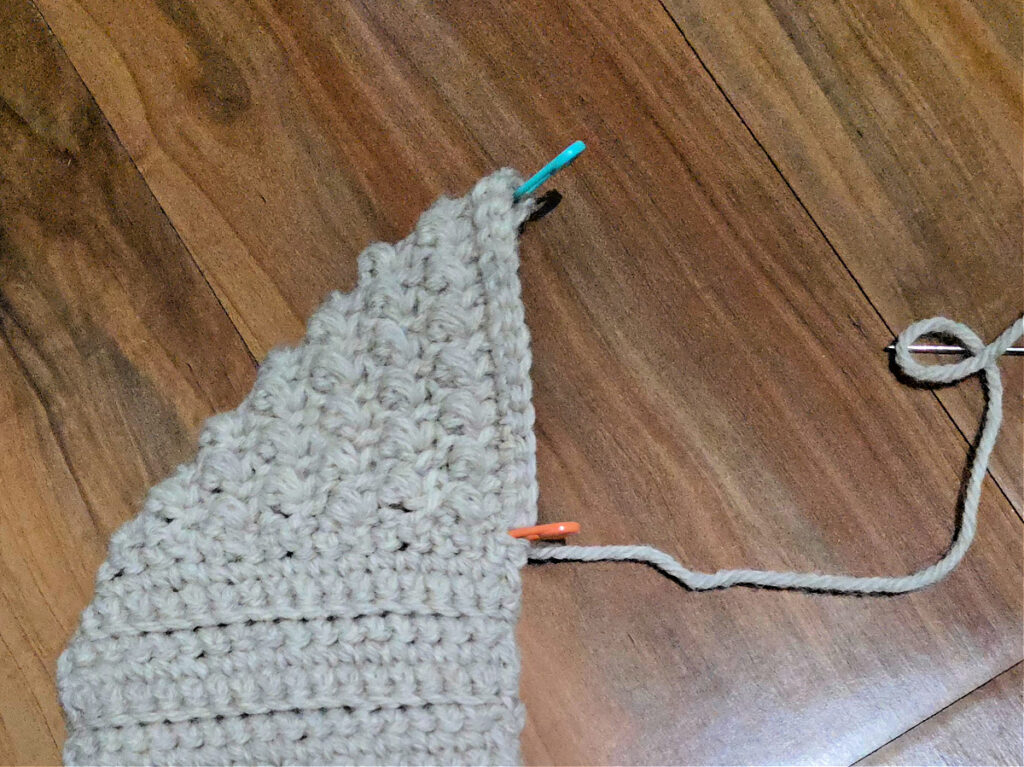 Seaming a grey crochet slipper against a wooden floor.