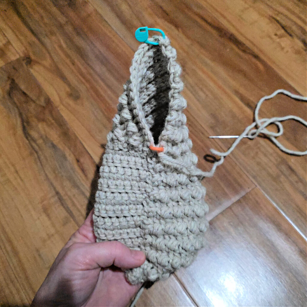Seaming a grey crochet slipper against a wooden floor.