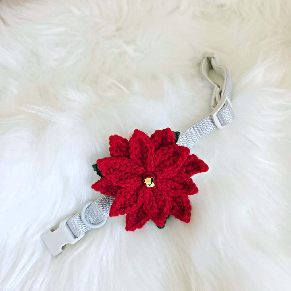 Close-up of a poinsettia crochet dog collar flower attached to a dog collar and laying on a fur blanket.