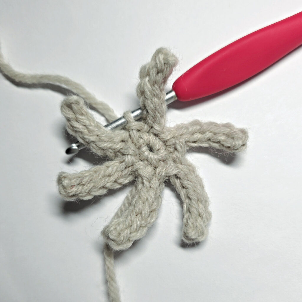 The second round of a crochet poinsettia flower made with a red crochet hook.