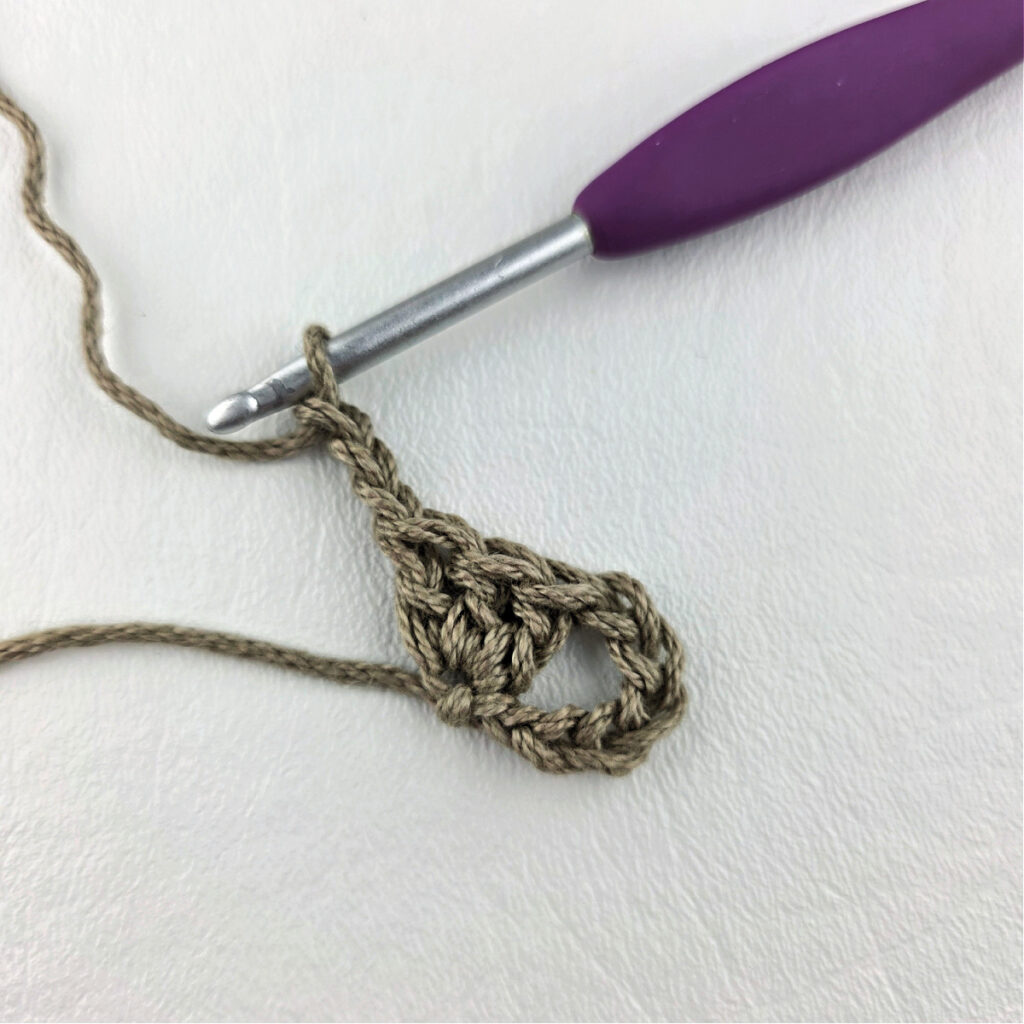 Round 1 of crochet granny stitch triangle with a purple crochet hook.
