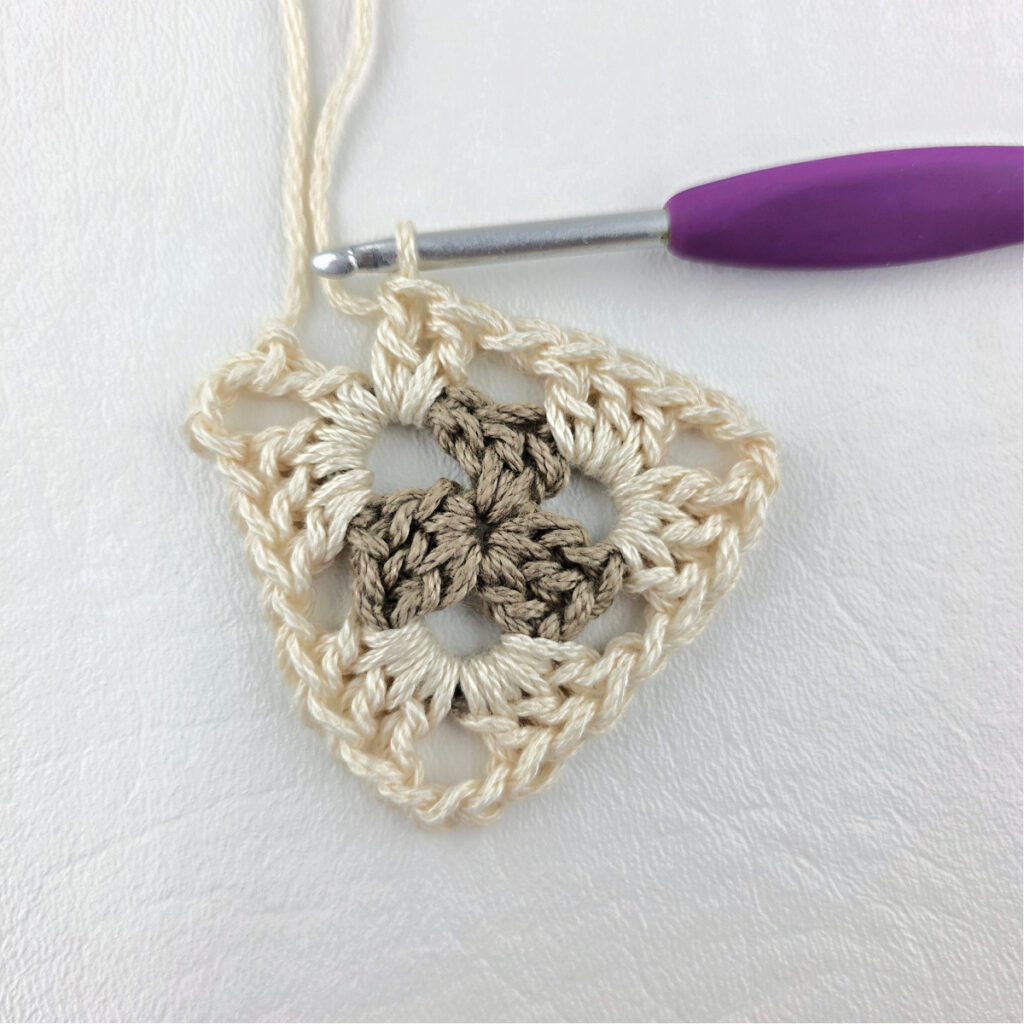 Round 2 of crochet granny stitch triangle with a purple crochet hook.